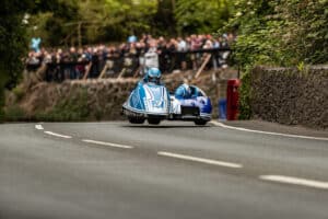 Isle of Man TT rider passing Braddan Bridge on a narrow village road 