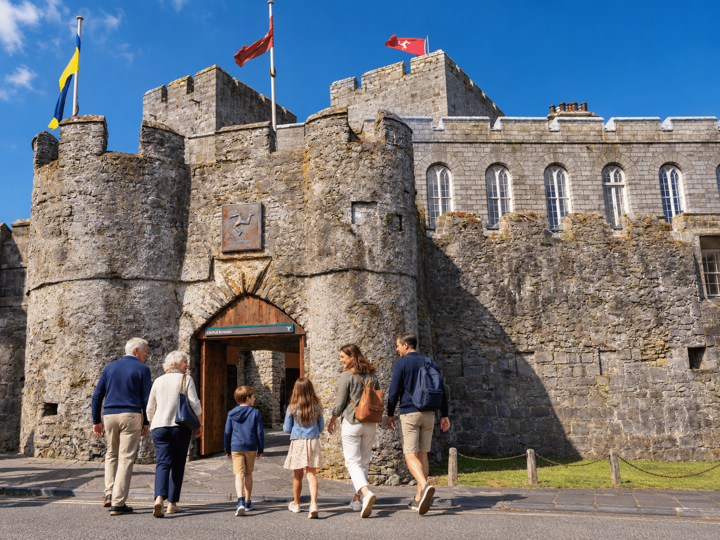 Multi-generational family walking towards the entrance of Castle Rushen in Castletown, Isle of Man.